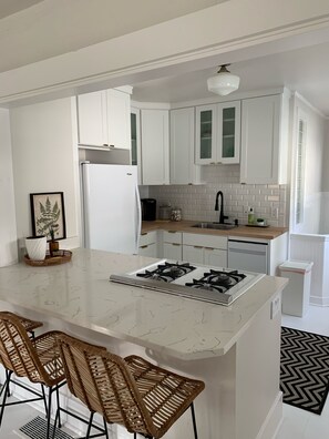 Una cocina moderna con armarios blancos, una isla central con taburetes de bar, una estufa a gas y un lavavajillas integrado.