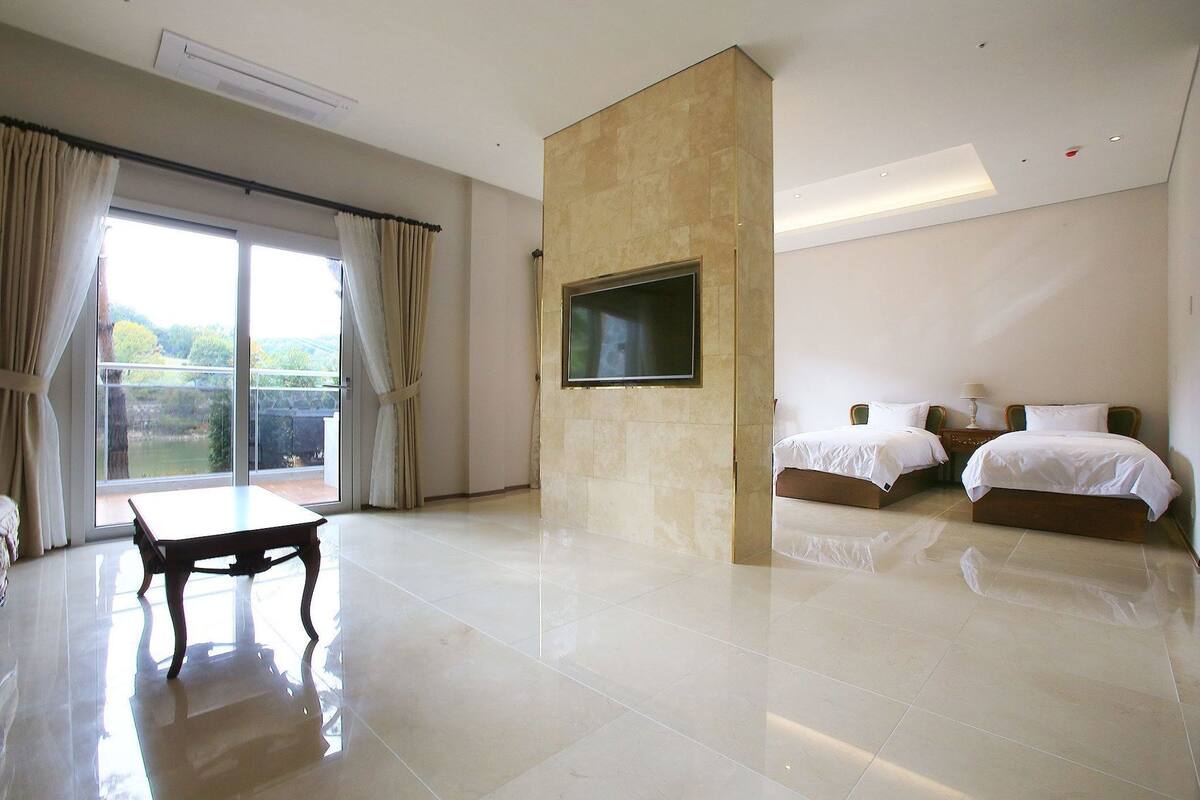 Habitación de hotel con un amplio ventanal corredero, un televisor de pantalla plana en la pared, dos camas con ropa blanca y una mesita.