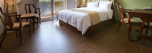 A bedroom with a large bed, wooden chairs, a small table, and a view through a glass door. - Hotel Gallery (Pocheon)