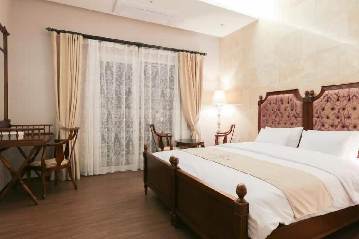 Una habitación de hotel con una cama de madera, un escritorio con una silla, un espejo y una ventana con cortinas.