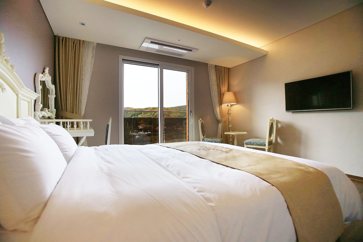 Habitación de hotel con una cama grande, un televisor en la pared y vistas al exterior a través de una puerta corrediza.