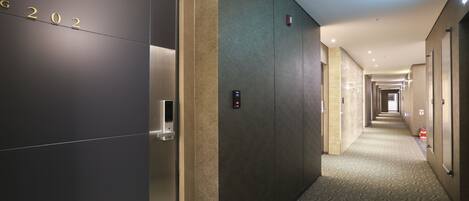 A hotel hallway with a modern design, featuring a carpeted floor and a series of doors on one side.