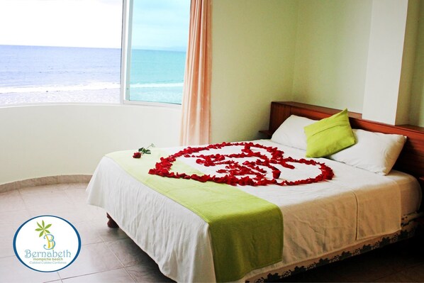 A hotel room with a bed, a view of the beach, and a logo on the wall.