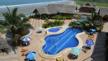 Relax by the ocean with a clear view from our pool surrounded by palm trees and thatched-roof structures.