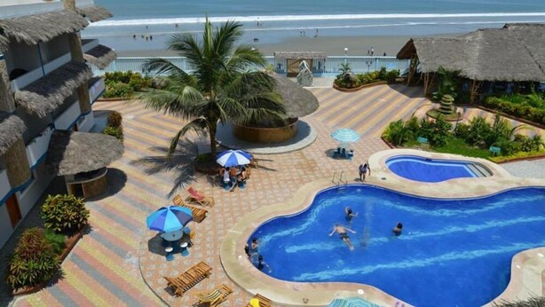 A resort with a swimming pool, beach view, and thatched-roof structures.