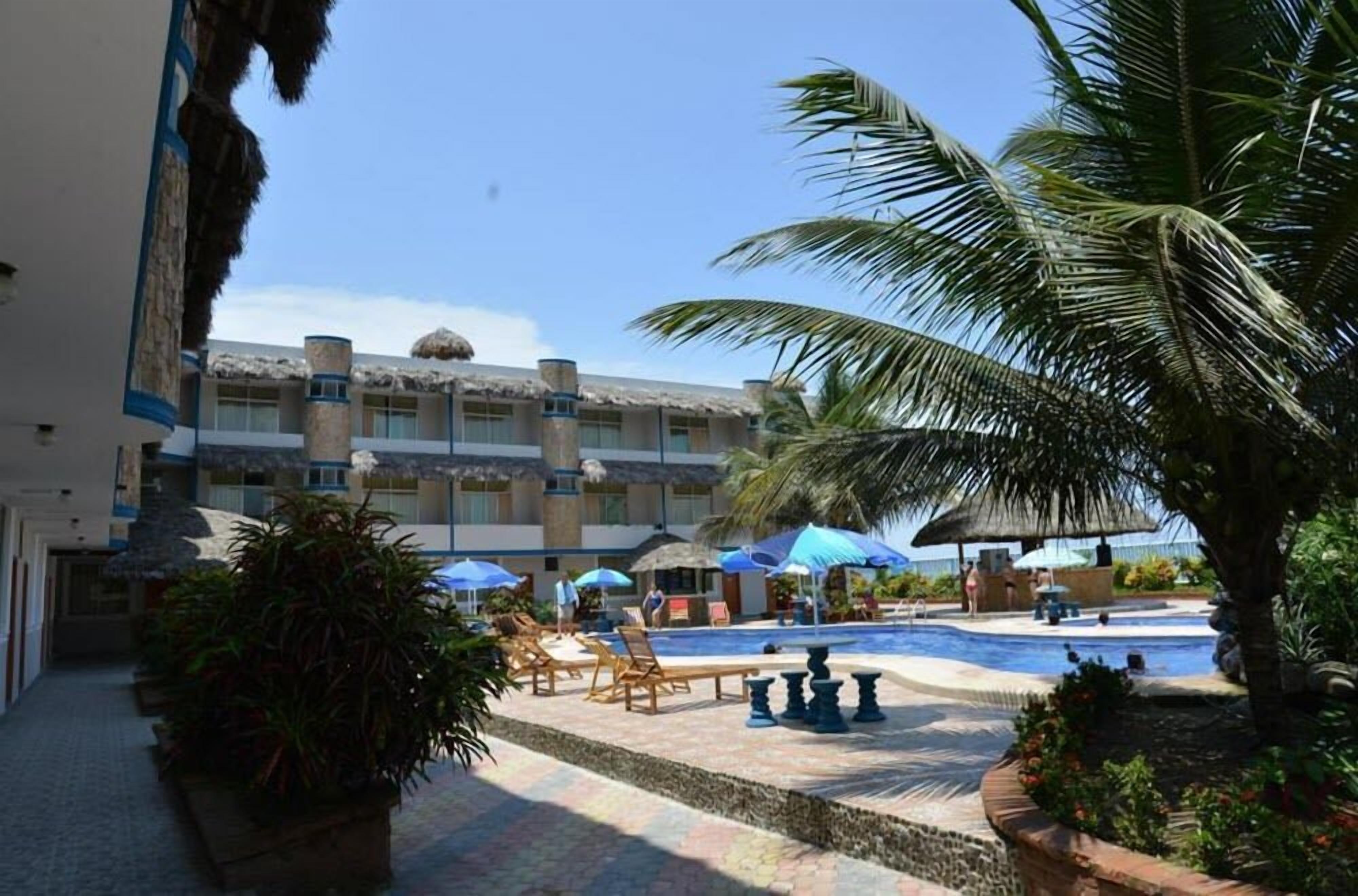 A hotel with a pool area, including lounge chairs and umbrellas, and a building with a thatched roof.