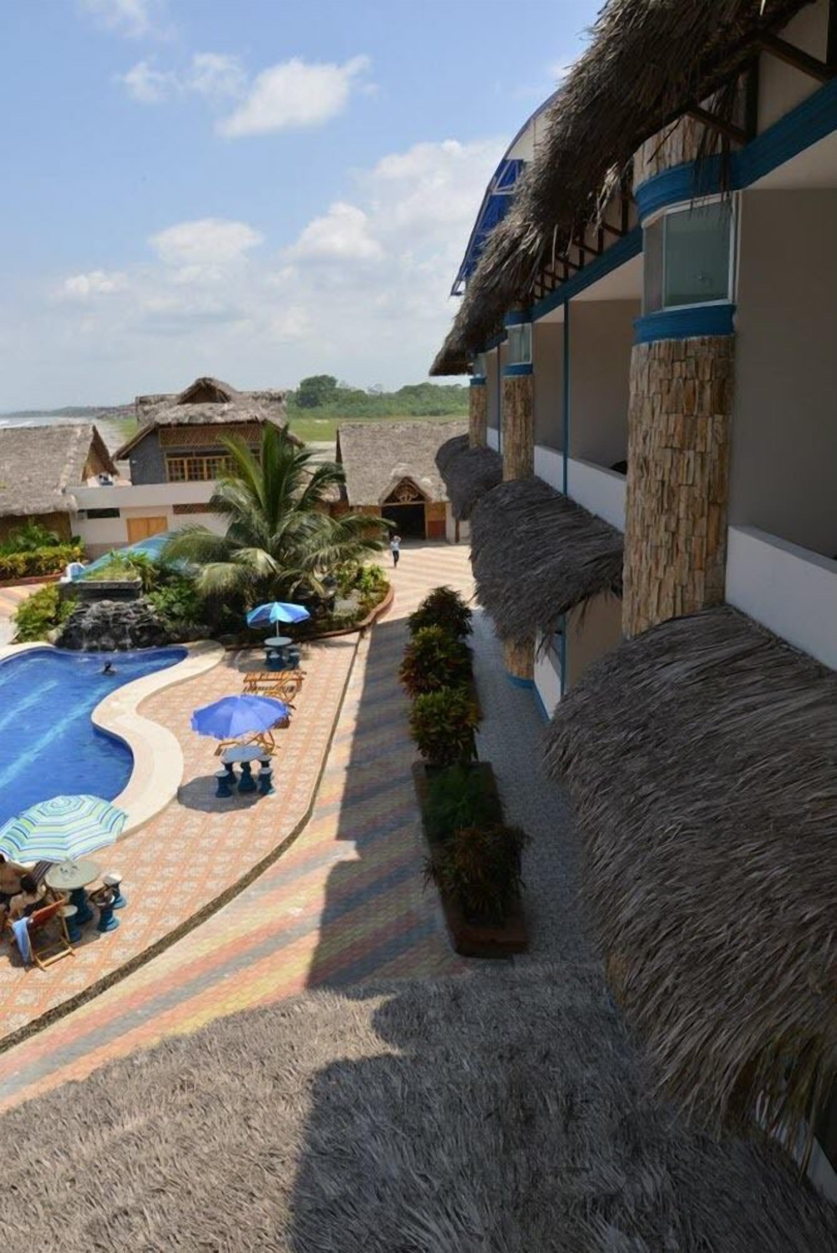 A resort with thatched-roof buildings, a swimming pool, and outdoor seating areas.