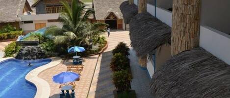 Un resort con edificios de techo de paja, una piscina y zonas de estar al aire libre.