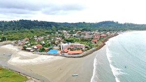 A coastal town with a beach, a large building with a red roof, and a rocky shoreline.
