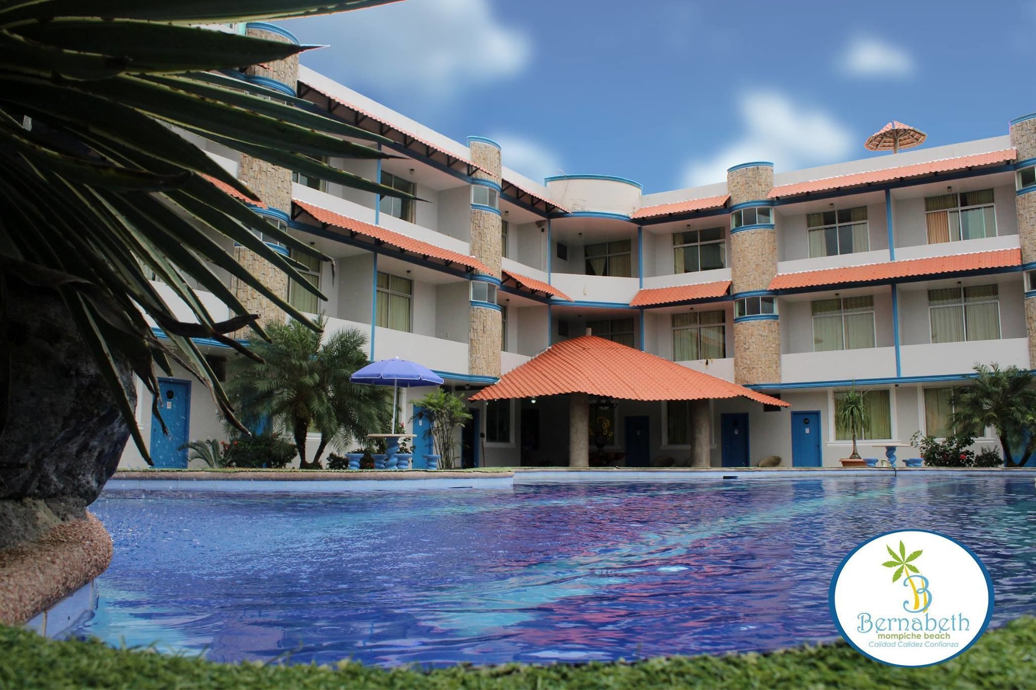 Un hotel con piscina, varios balcones y un jardín tropical.