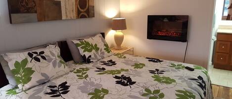 A bedroom with a bed, a nightstand with a lamp, a television, and a wall with abstract art.