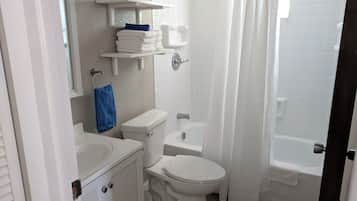 A bathroom with a toilet, sink, and bathtub. There are shelves above the toilet and a shower curtain.
