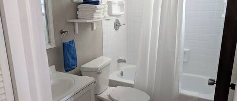 A bathroom with a toilet, sink, and bathtub. There are shelves above the toilet and a shower curtain.