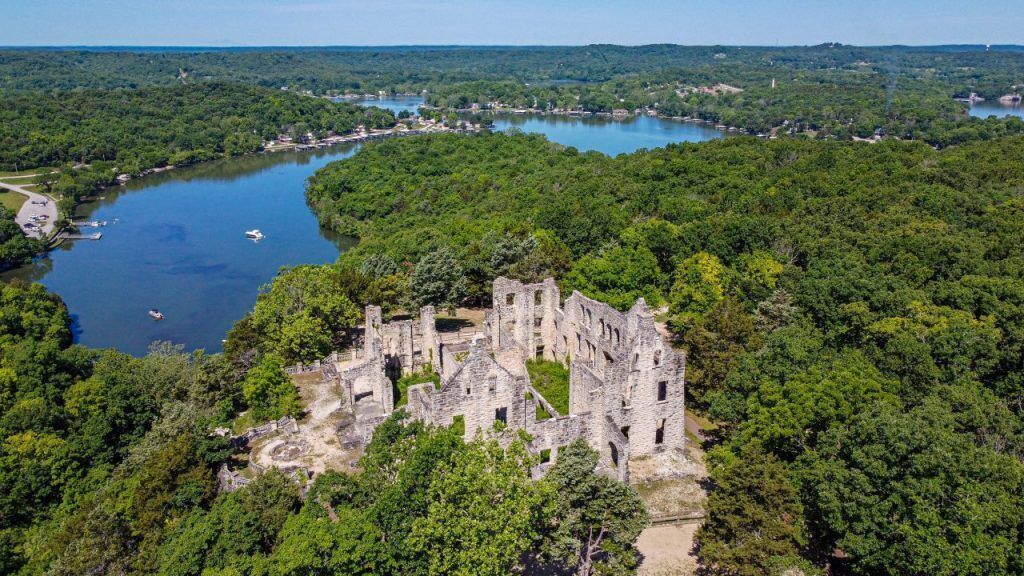 An aerial view of a historic stone castle surrounded by dense forest and a river.