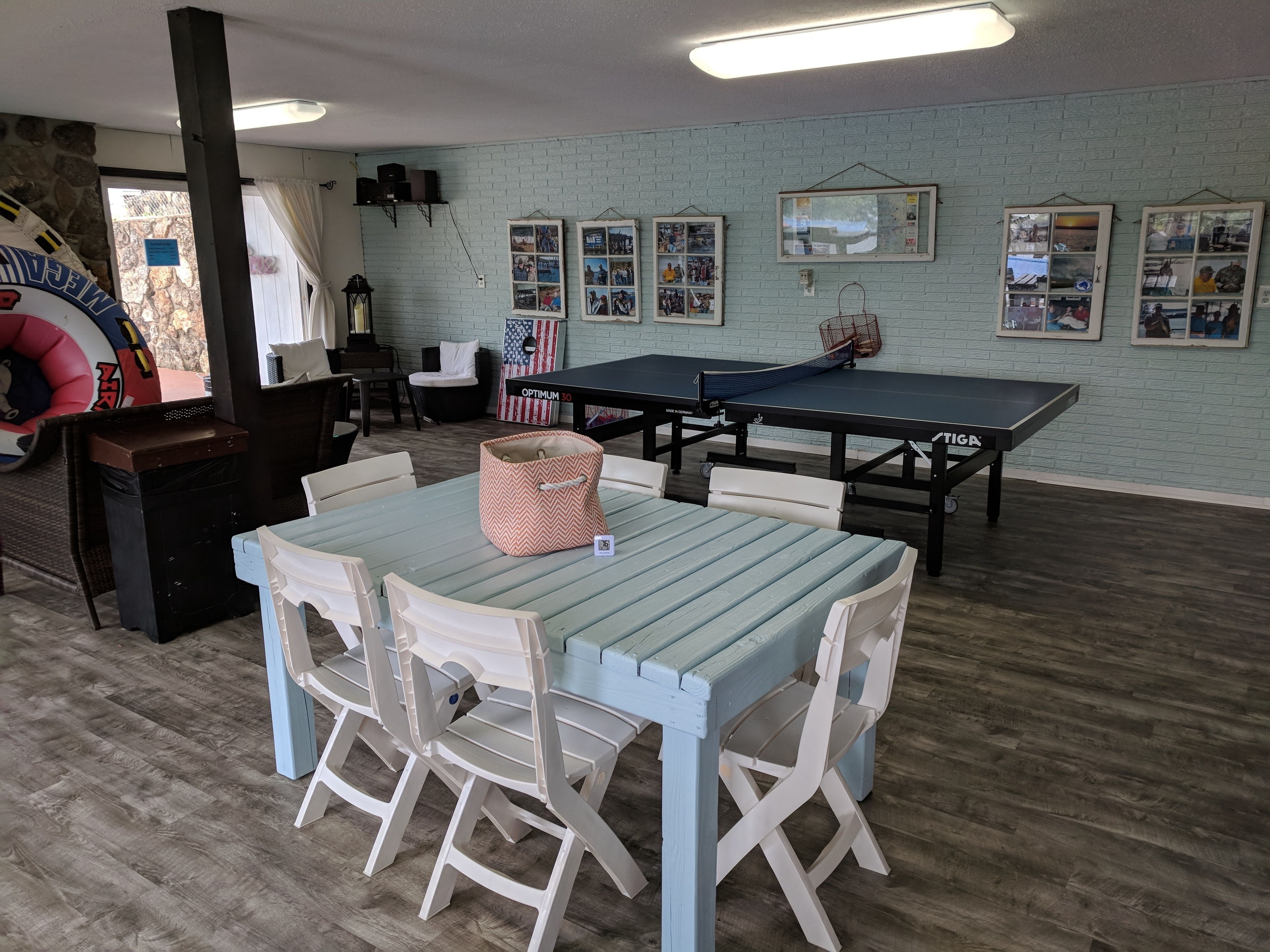 A room with a ping pong table, chairs, a small table with a basket, and framed pictures on the wall.
