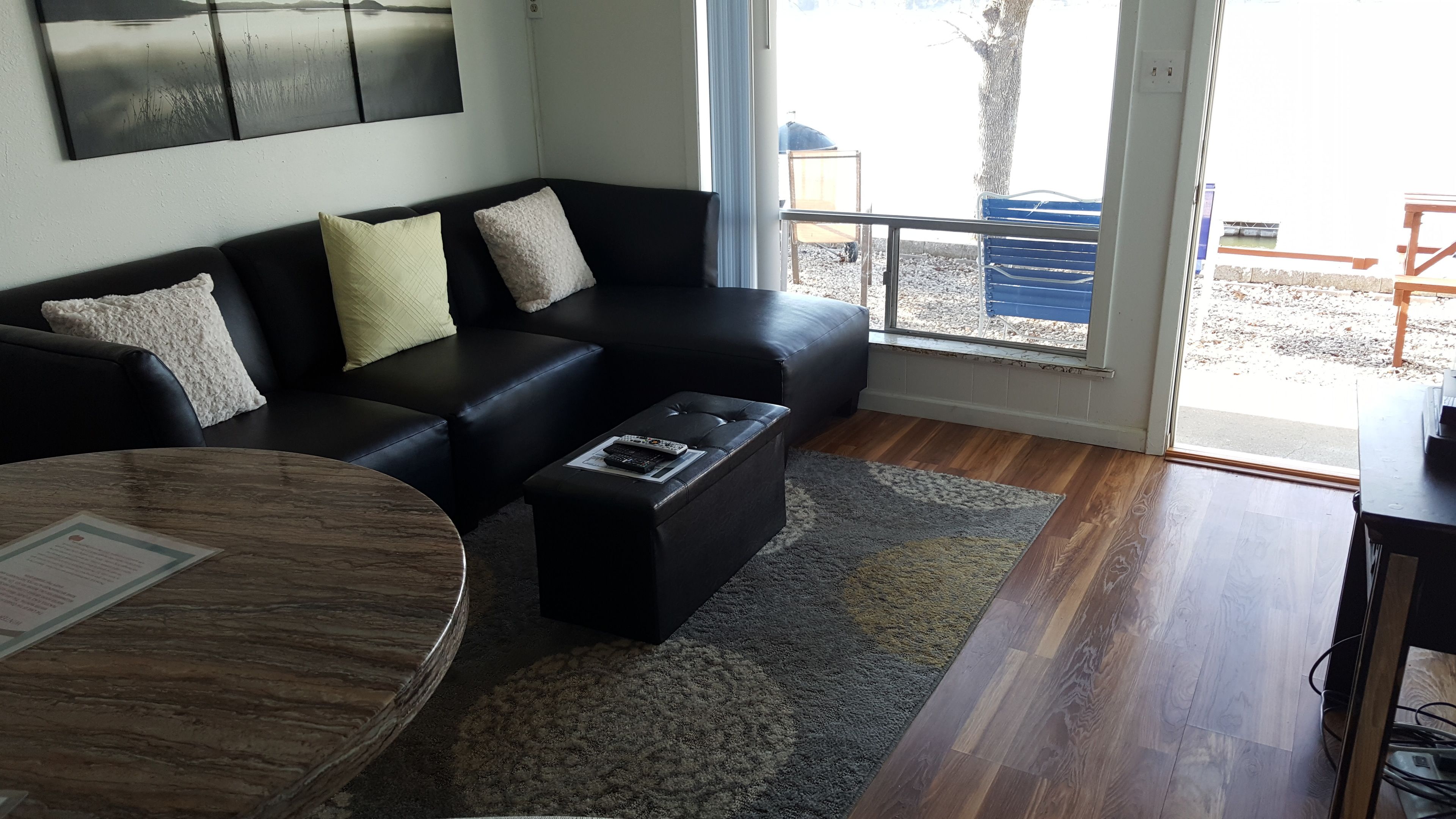 A modern living room with a black leather sofa, a round coffee table, and a view of the outdoors through a glass door.