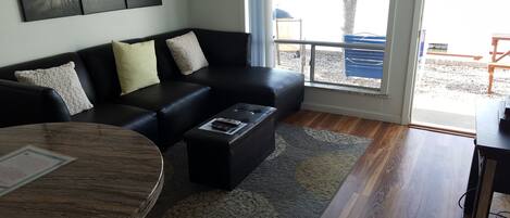 A modern living room with a black leather sofa, a round coffee table, and a view of the outdoors through a glass door.