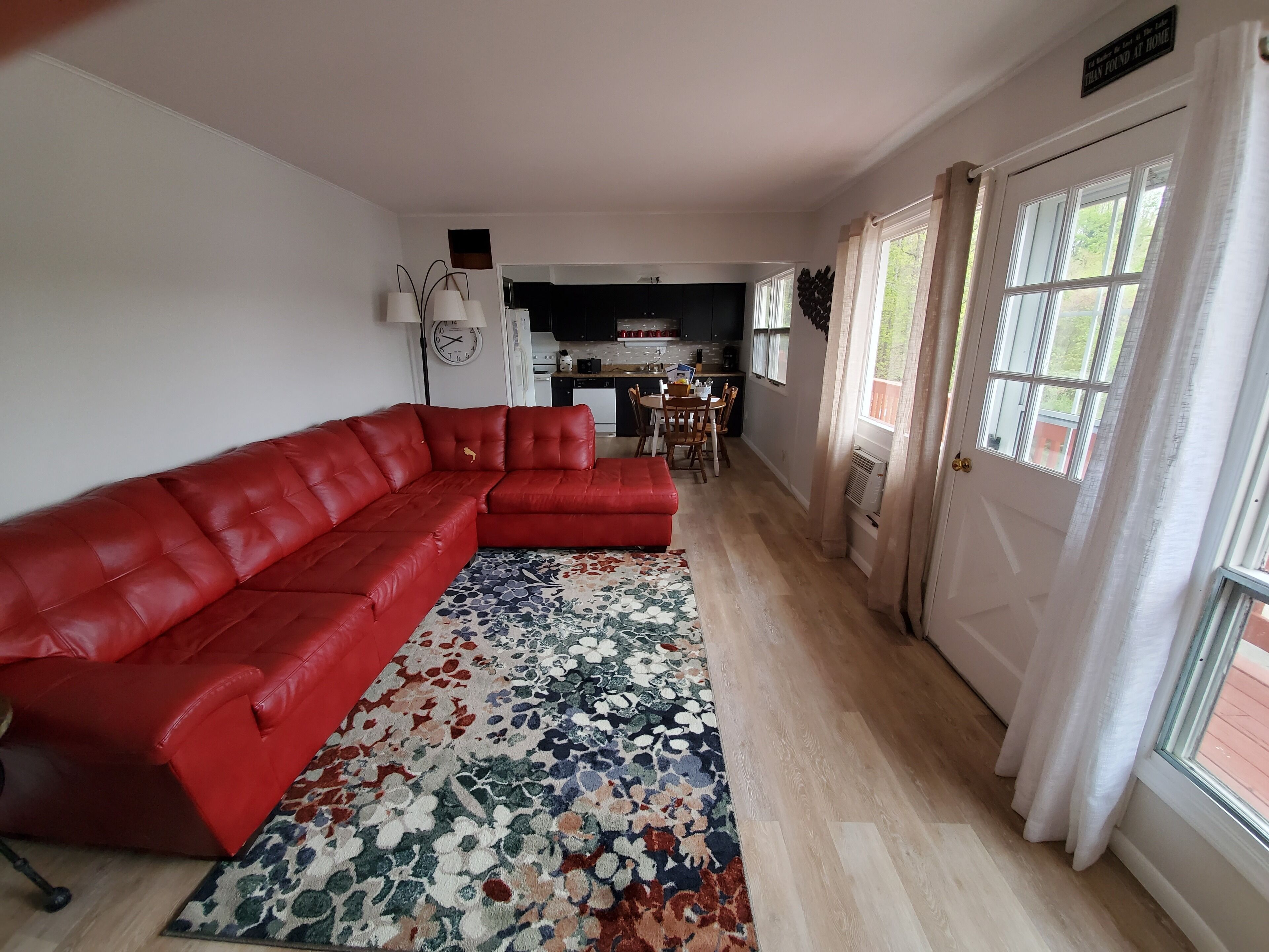Una sala de estar con un sofá modular rojo, un tapete estampado y una cocina al fondo.