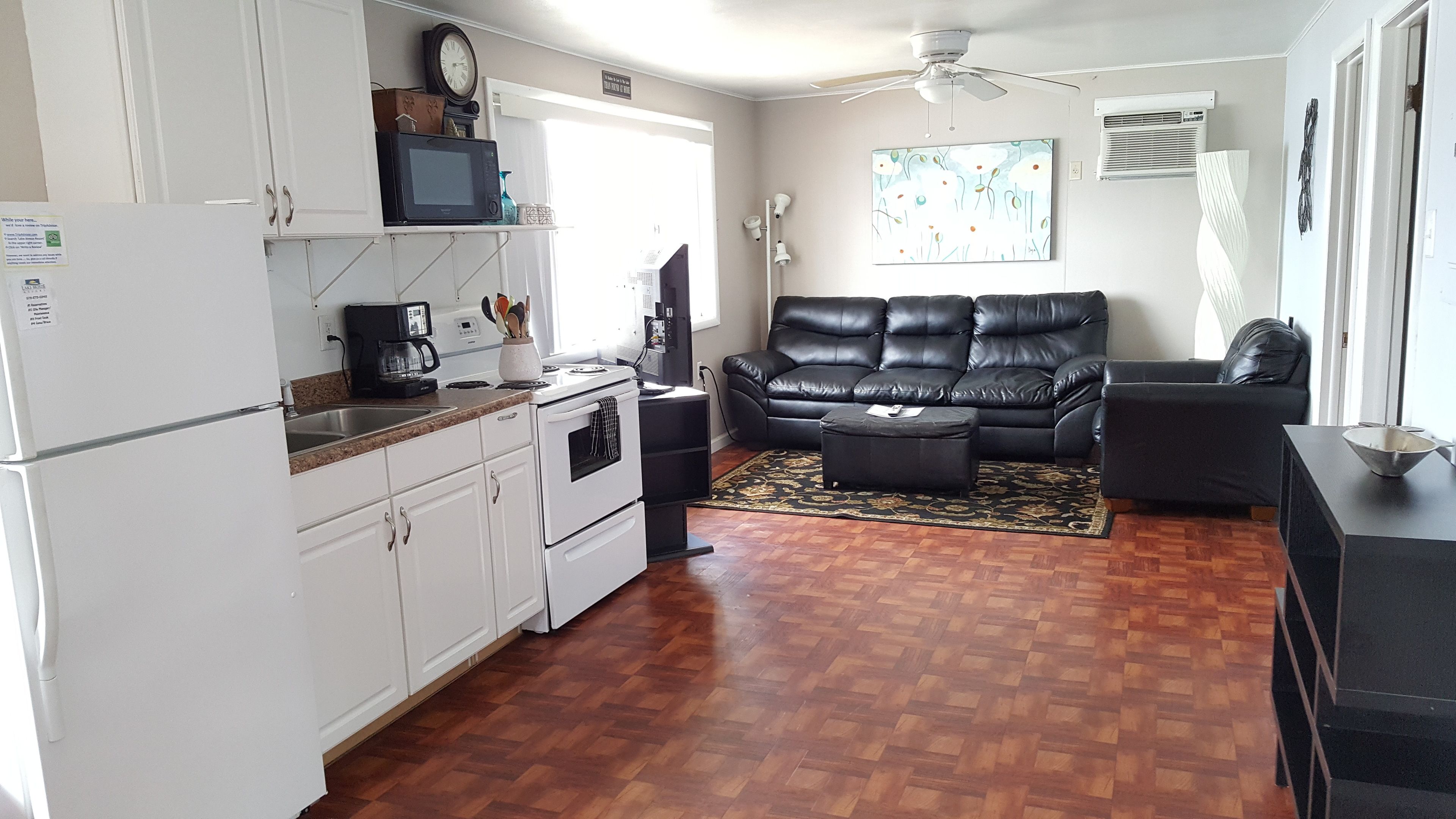 A compact living space with a kitchenette, a black leather sofa, a coffee maker, and a decorative rug.