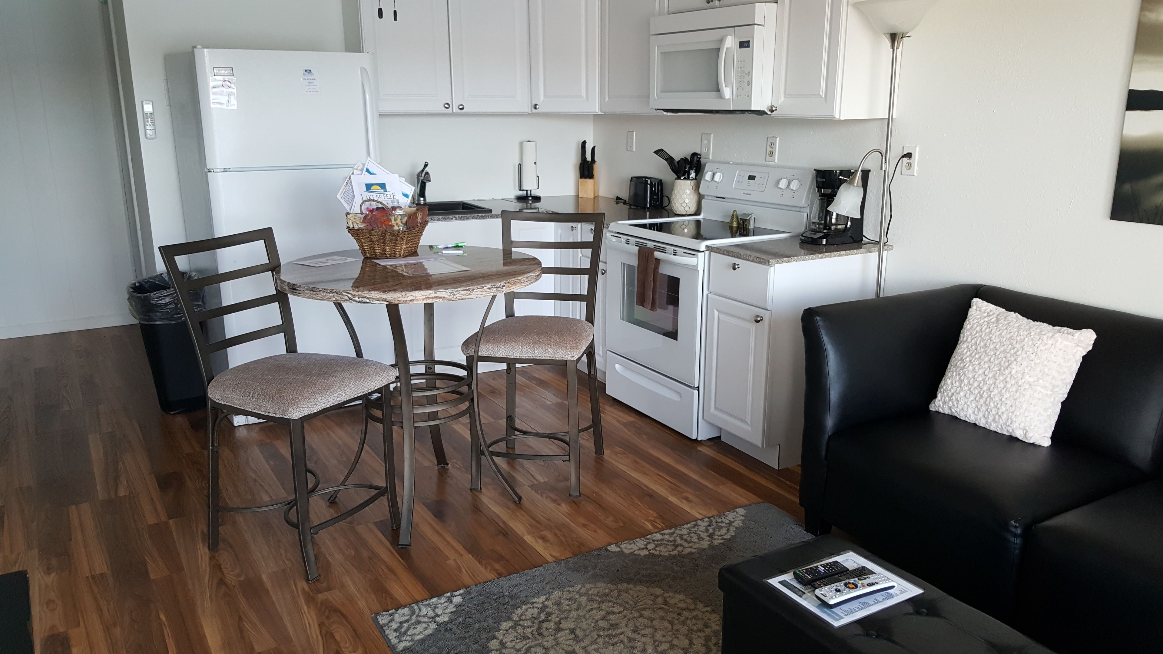 A compact kitchen with a dining table, chairs, a black leather sofa, and a small coffee table.