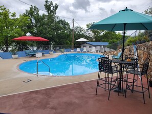 A swimming pool with lounge chairs and umbrellas, surrounded by a stone wall and trees. - Lake Breeze Resort  (Camdenton)