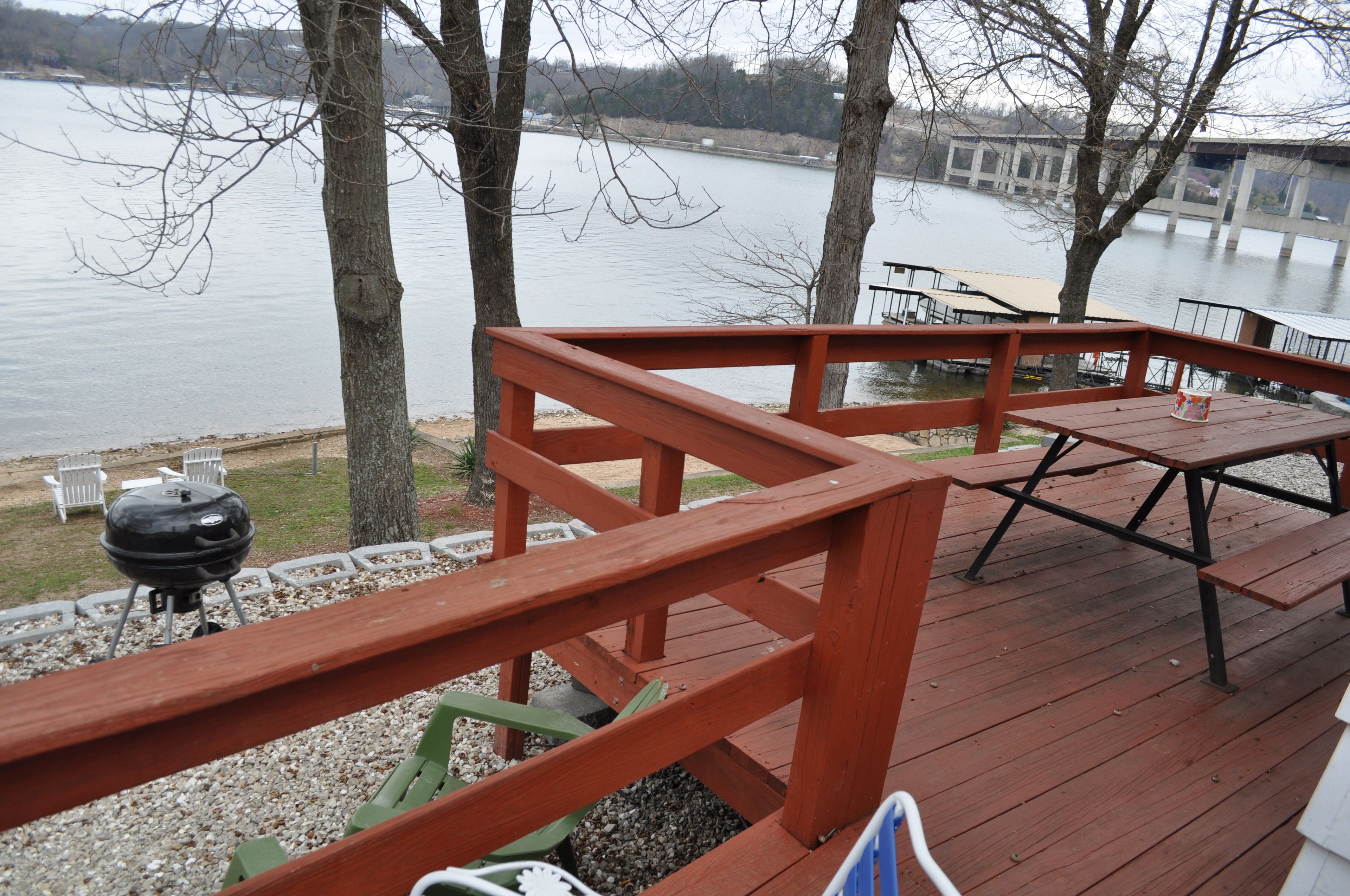 A wooden deck with picnic tables and a barbecue grill overlooking a lake.