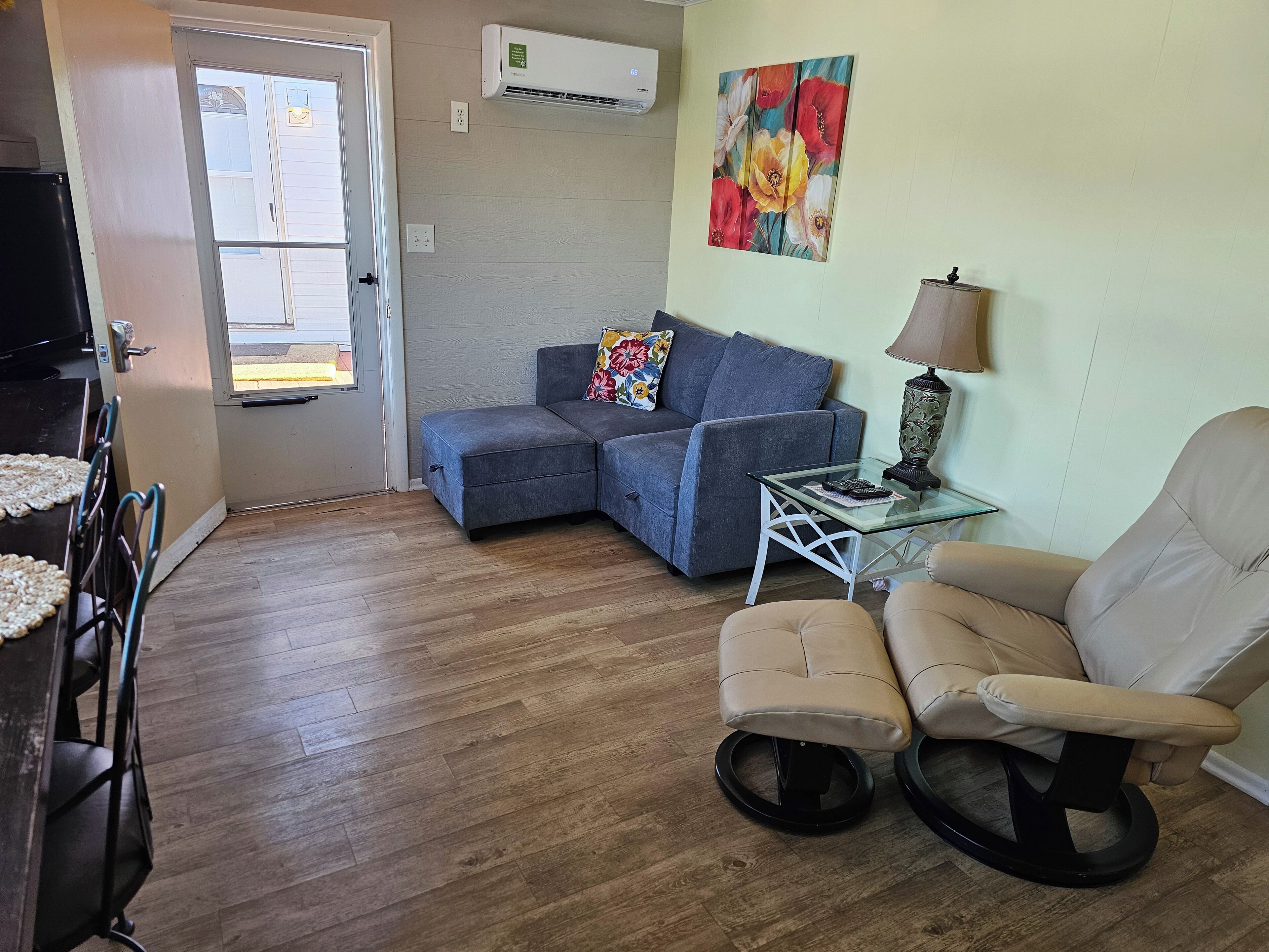 A living room with a sectional sofa, a glass coffee table, a beige armchair, and a painting on the wall.