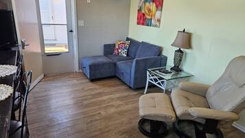 Una sala de estar con un sofá seccional, una mesa de centro de vidrio, un sillón color beige y un cuadro en la pared.