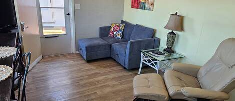 A living room with a sectional sofa, a glass coffee table, a beige armchair, and a painting on the wall.