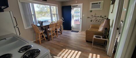 A compact kitchen with a stove, dining table with chairs, a sofa, and a ceiling fan.