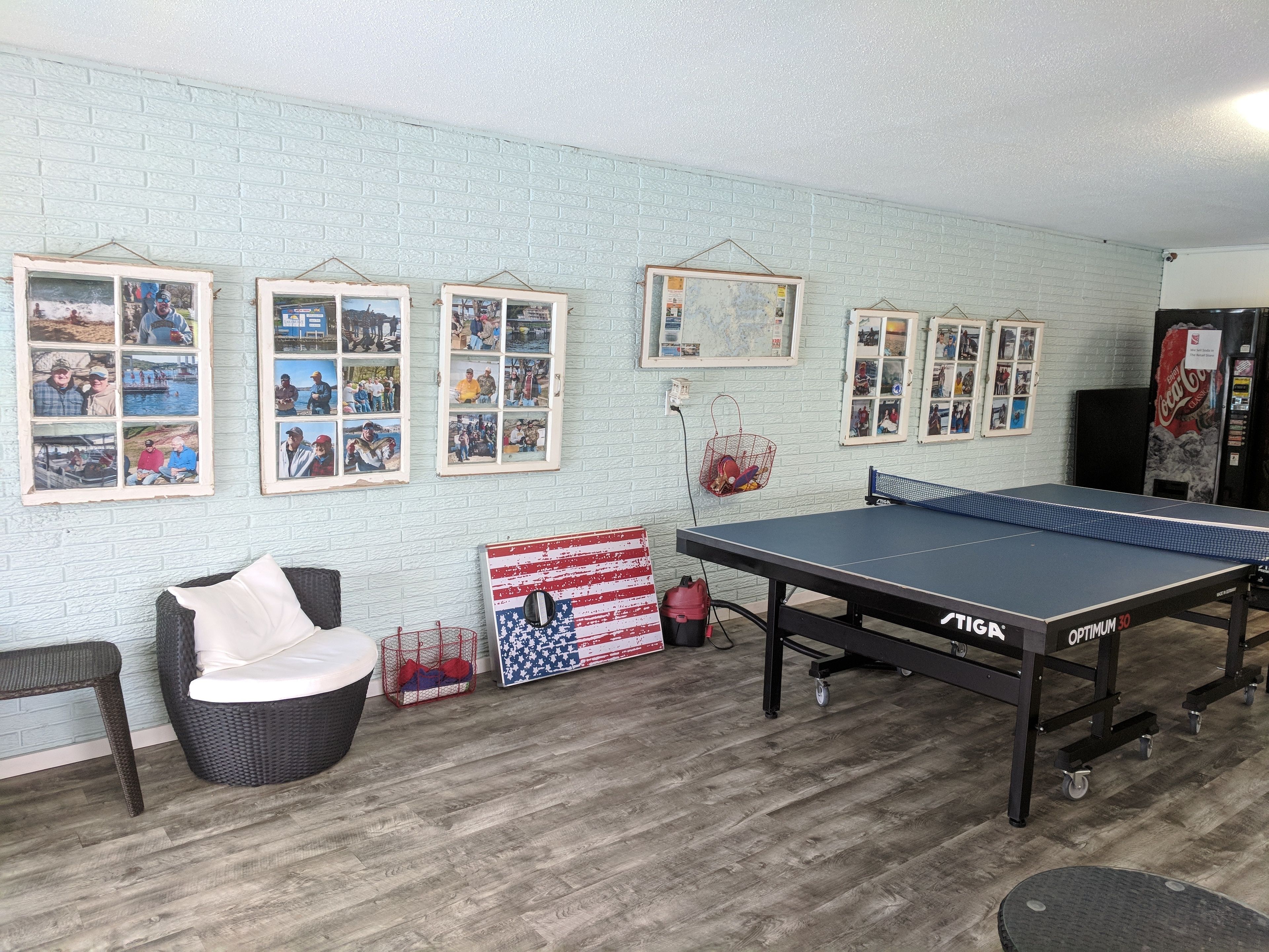 A room with a ping pong table, wicker furniture, and framed pictures on the wall.