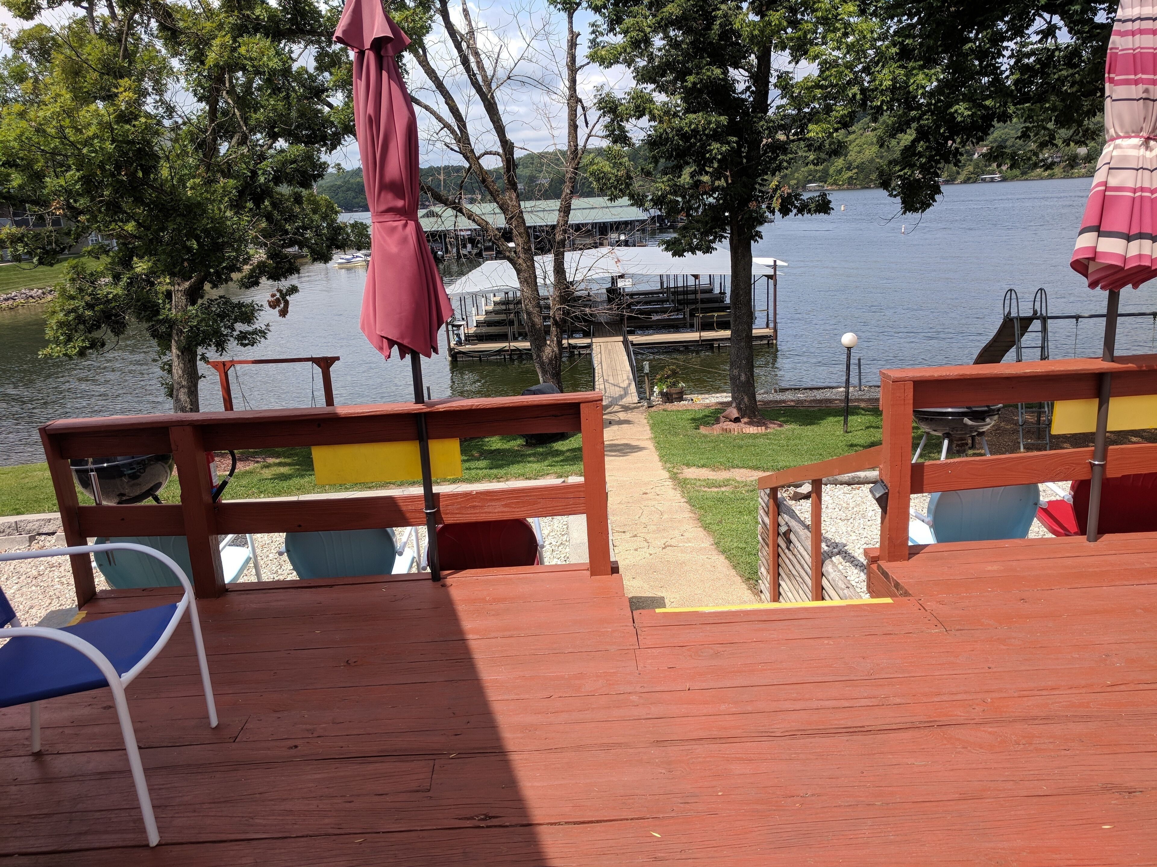 A wooden deck with chairs and a table, overlooking a lake with boats and docks in the background.