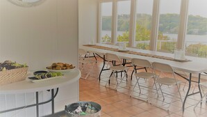 A dining area with a table set for six, chairs, a buffet table with food, and a view of a lake through large windows. - Lake Breeze Resort  (Camdenton)