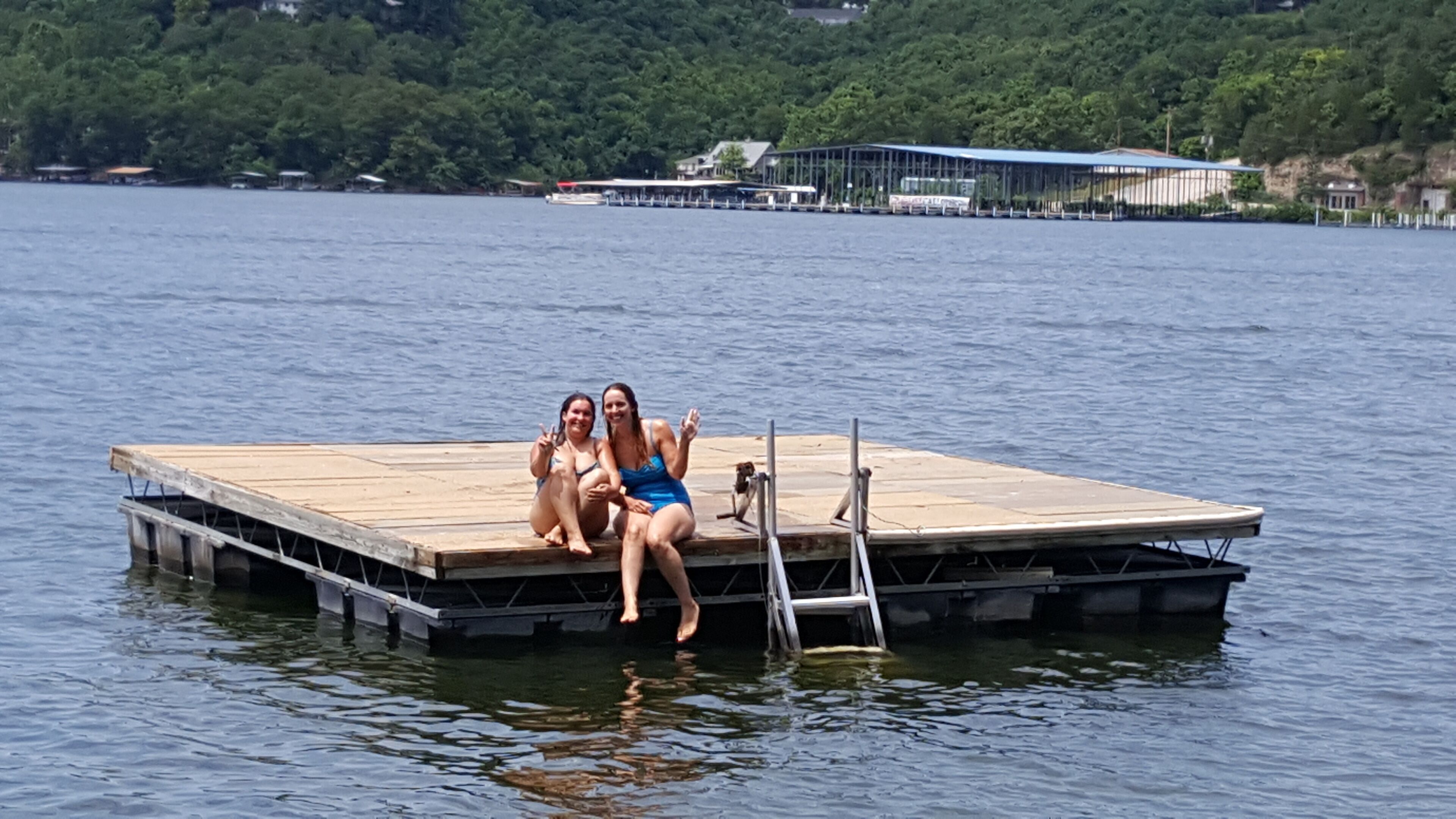 Eine Holzstege ragt in einen See, auf dem zwei Personen sitzen.