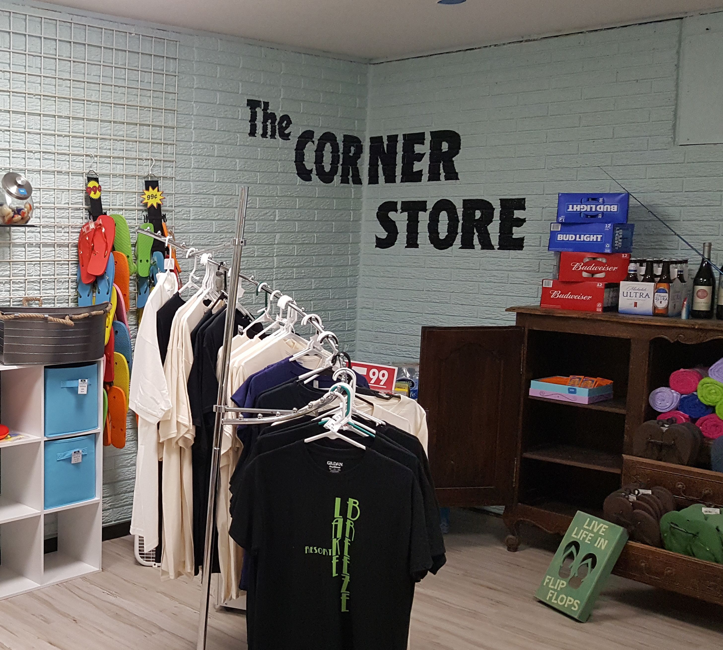 Un negozio di abbigliamento con un espositore di camicie, un cartello che riporta 'The Corner Store' e scaffali con scarpe e borse.