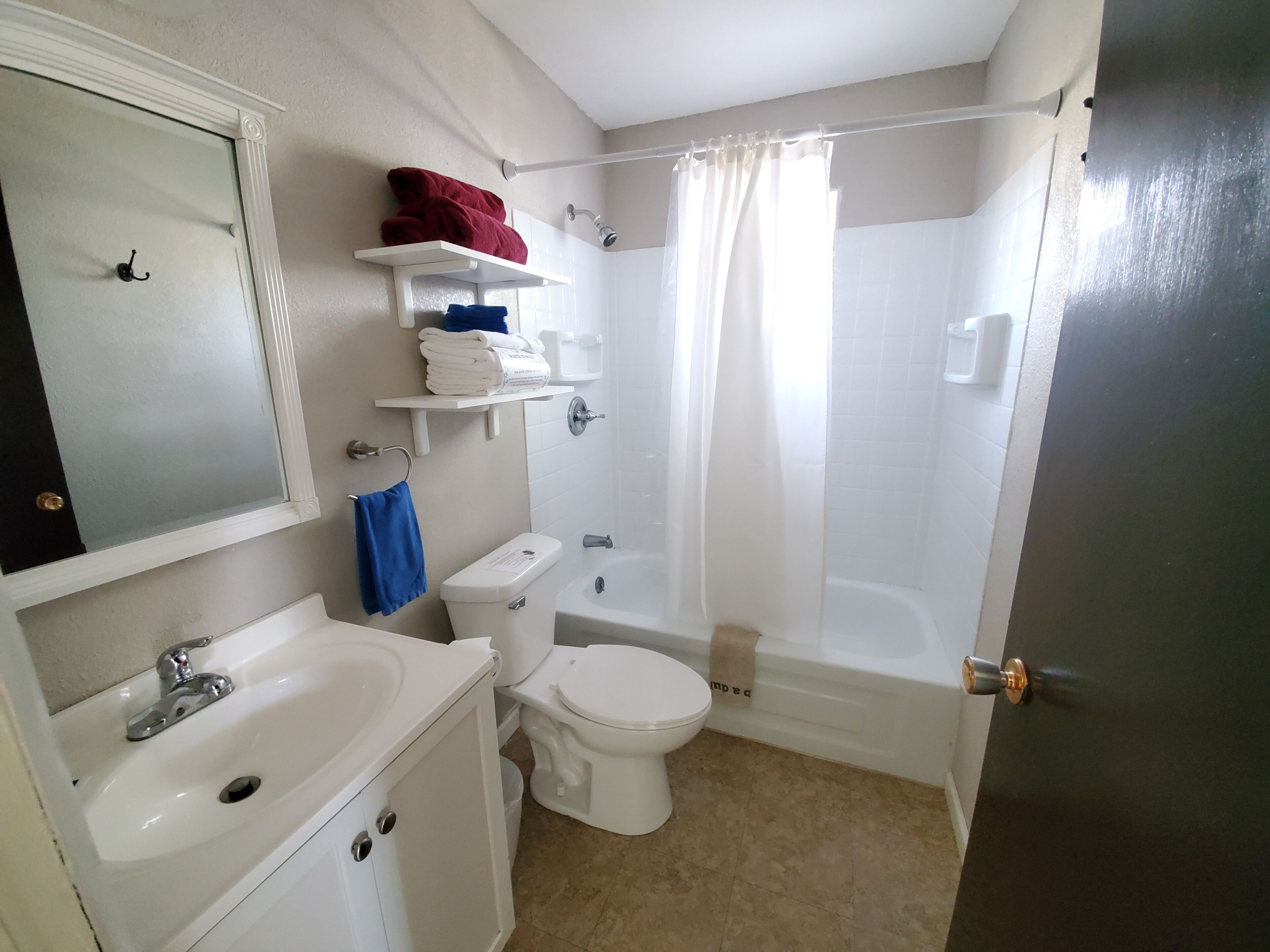 A bathroom with a sink, toilet, and bathtub. There are shelves with towels and a mirror above the sink.