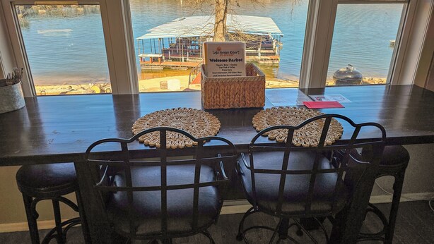 A dining area with a view of a lake, a sign for Lignite Lodge Resort, and a basket of items on the table. - Lake Breeze Resort  (Camdenton)
