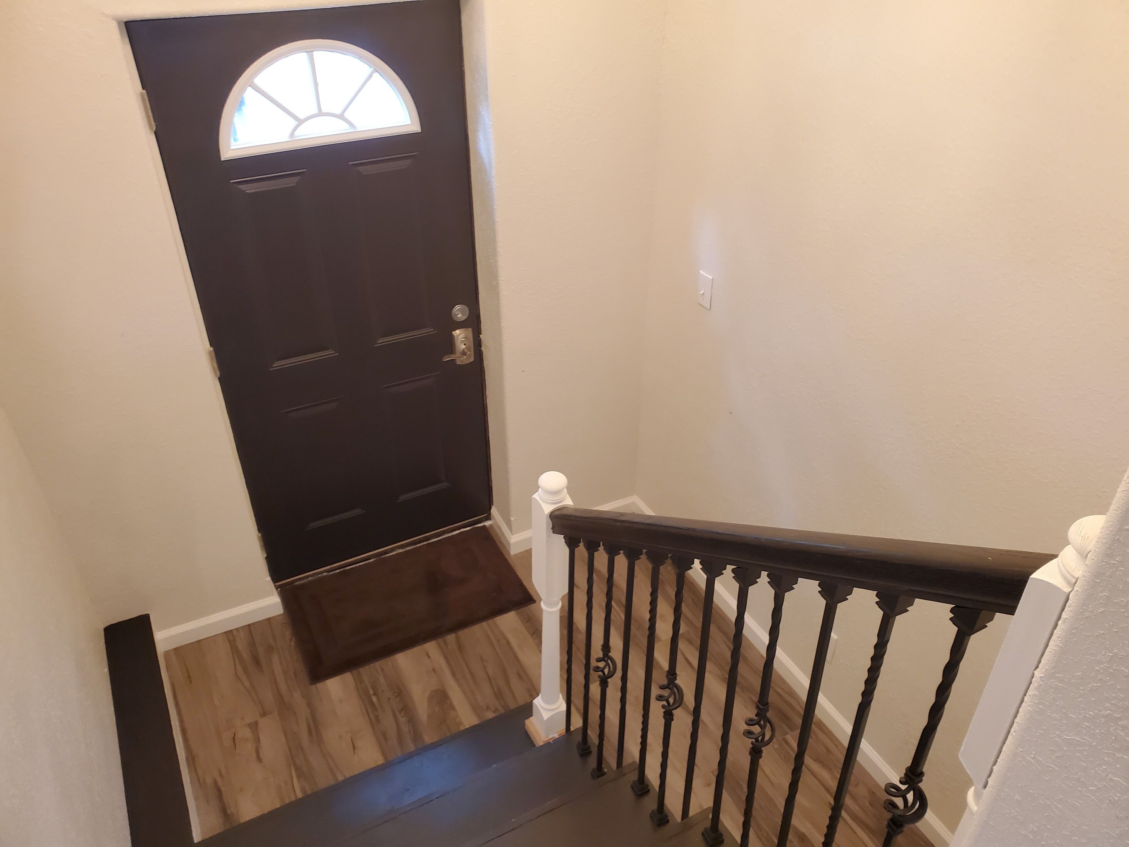 A dark wooden door with a small window, a wooden staircase with a white balustrade, and a light-colored wall.