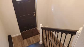 A dark wooden door with a small window, a wooden staircase with a white balustrade, and a light-colored wall.