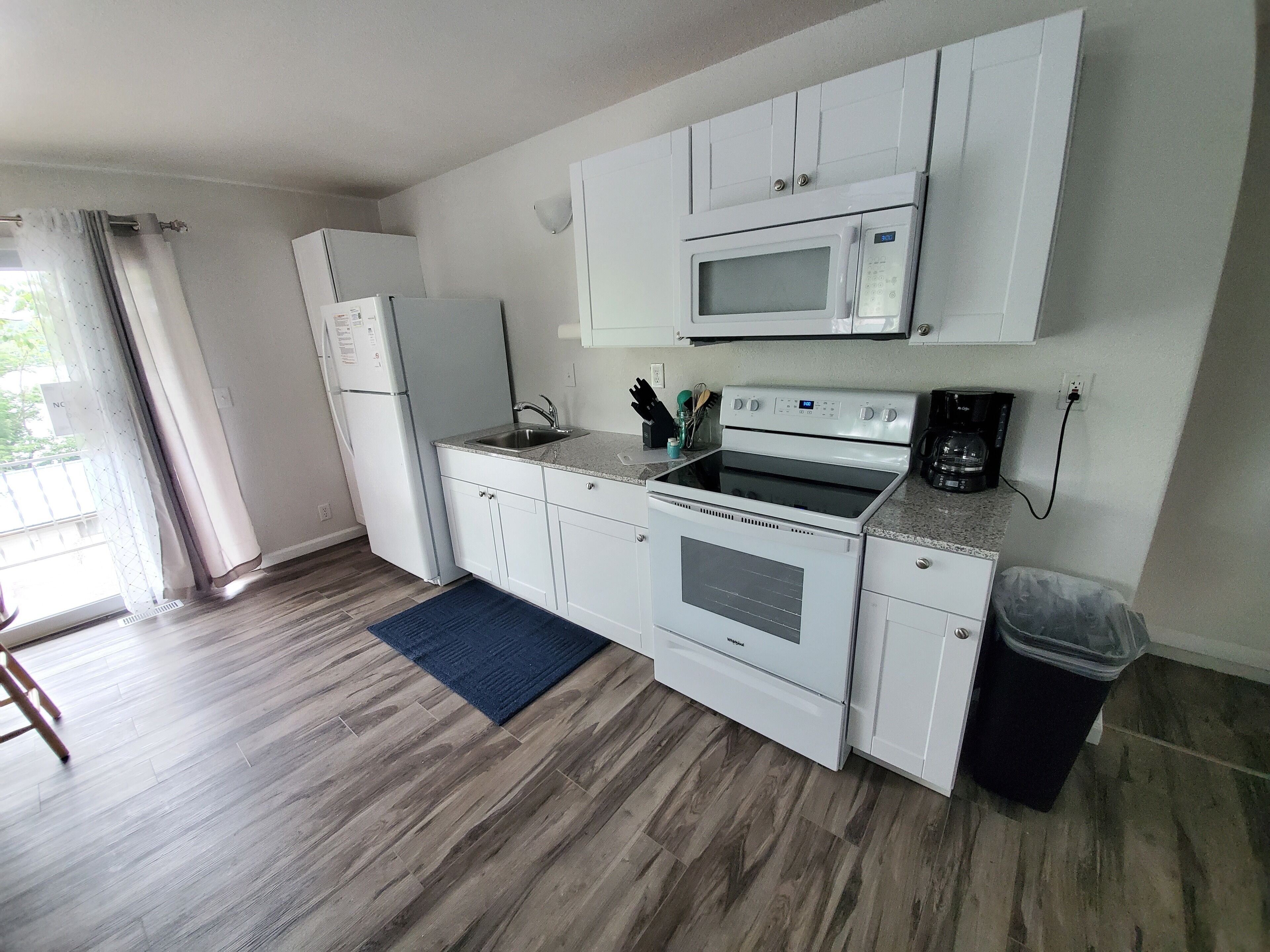 Una cocina compacta con armarios blancos, microondas integrado, estufa y refrigerador.