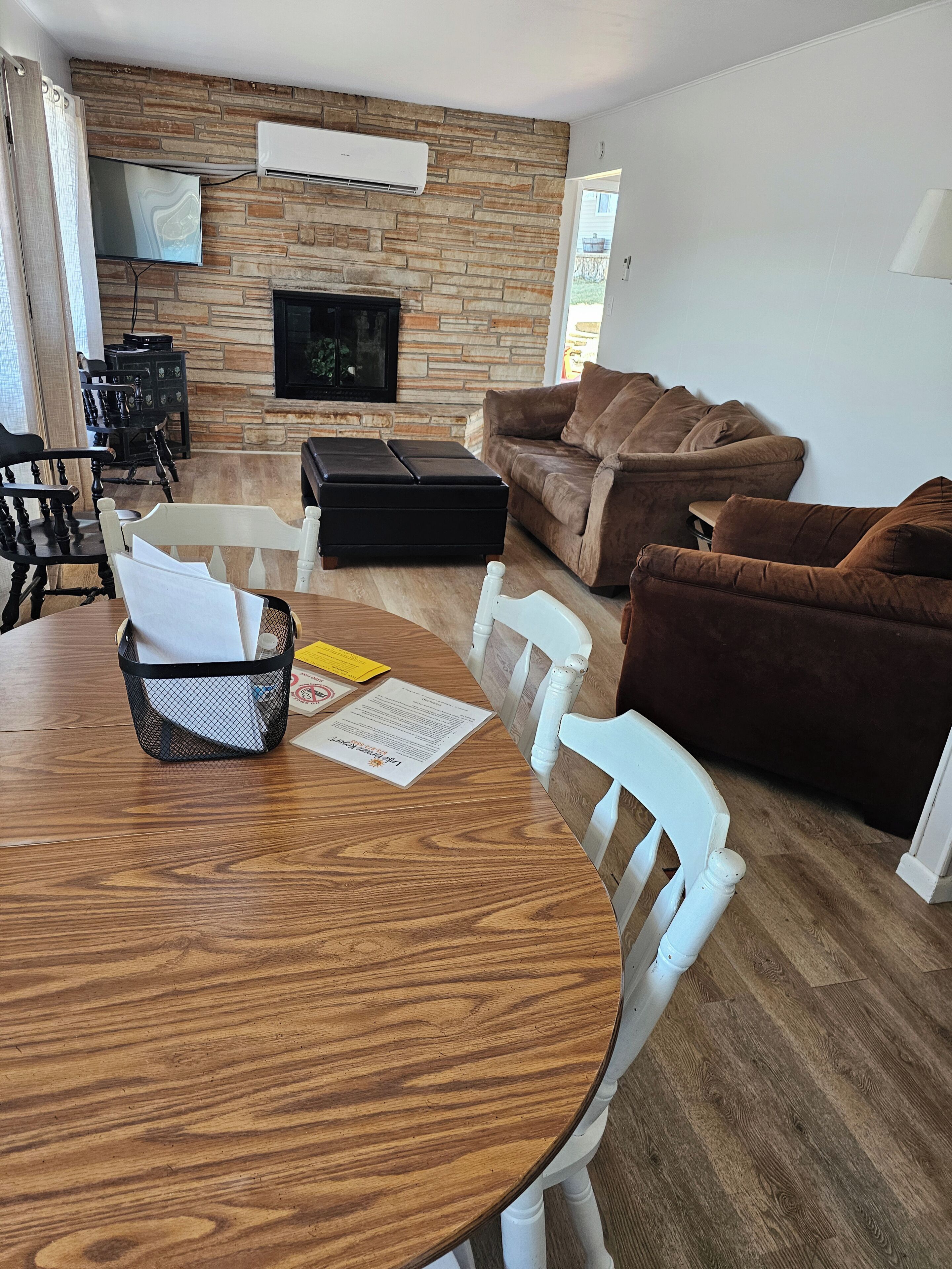 A living room with a stone wall, a flat-screen TV, a brown sofa, a white chair, and a wooden dining table.
