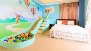 Zona de juegos infantiles con un tobogán, una piscina de pelotas y un mural de un molino de viento y globos aerostáticos.