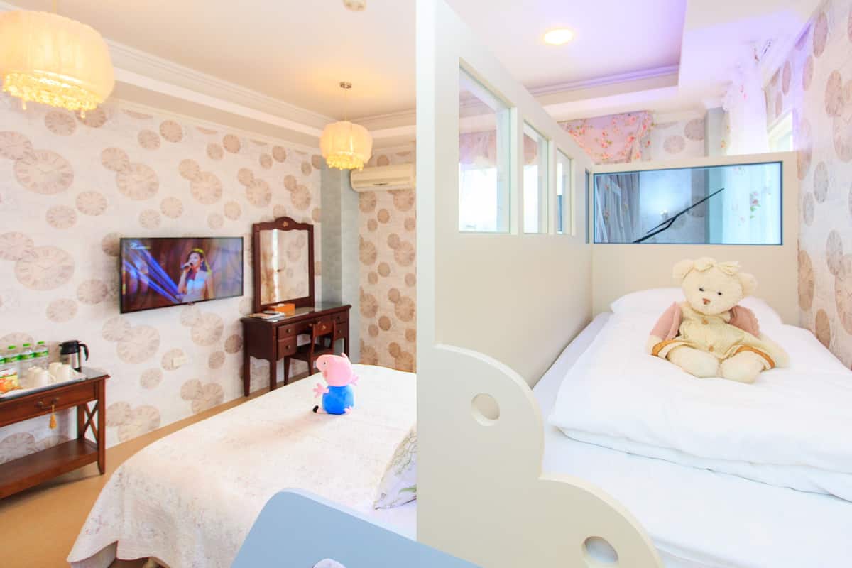 A hotel room with a bed, a desk, a television, and a teddy bear.