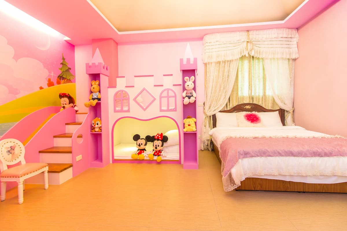 A pink-themed children's room with a bed, a small chair, a staircase, and a wall decorated with Mickey Mouse figures and a castle.