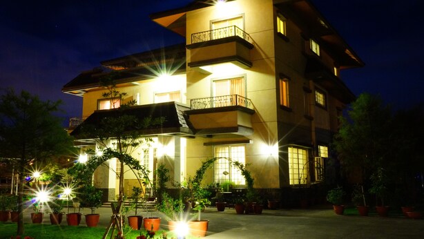 Un hotel de varios pisos con balcones, plantas en macetas y una fachada bien iluminada.