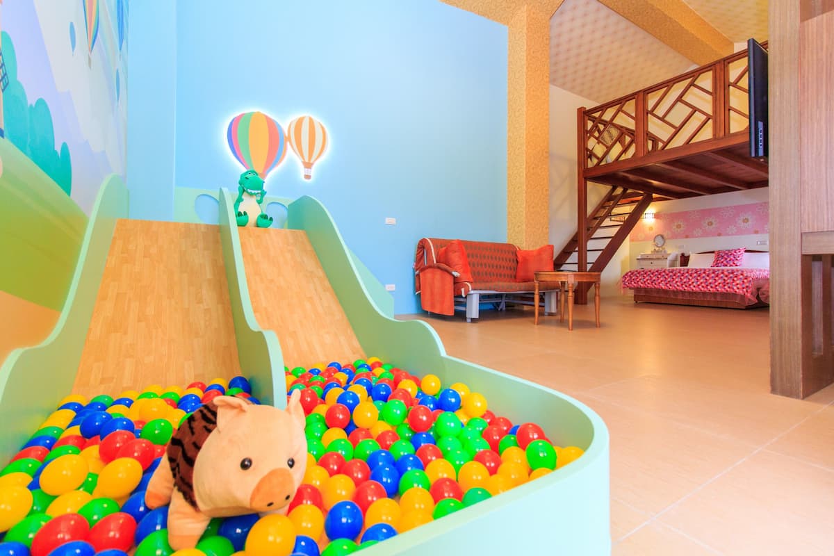 A play area with a slide and ball pit, a staircase, and a bed with a pink and white checkered bedspread.