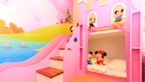 Una habitación infantil con temática rosa, adornada con personajes de Mickey y Minnie Mouse, un tobogán y una cama con ropa de cama blanca.