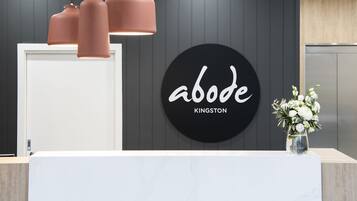 A reception desk with a black circular sign reading "abode KINGSTON" and a vase with white flowers.