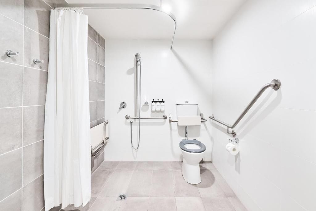 A modern bathroom with a shower, toilet, and grab bars.