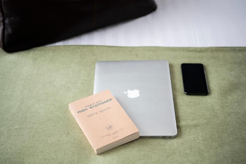 Una laptop, un teléfono inteligente y una libreta sobre una superficie de tela verde.